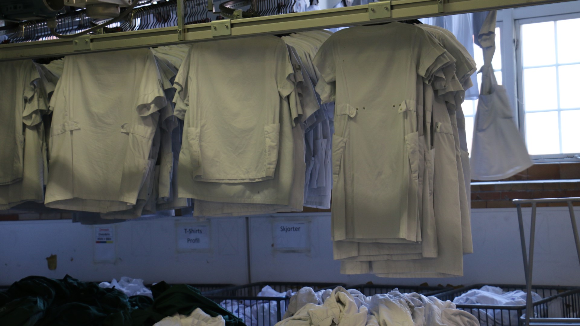 Row of hanging white t-shirts in front of a white wall with a window in the right